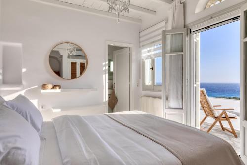 a white bedroom with a large bed and a mirror at Villa Ainar in Tinos