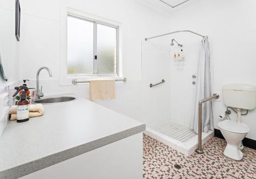 a white bathroom with a shower and a sink at Beachfront Gerroa in Gerroa