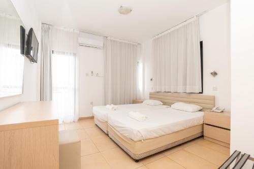 a white bedroom with a bed and a desk at Flora Hotel Apartments in Protaras