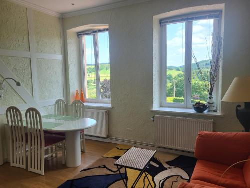 a living room with a table and three windows at Die Alte Schule app in Saint-Vith