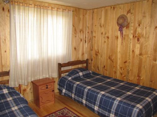 1 dormitorio con 2 camas y pared de madera en Hostal Austral, en Ancud