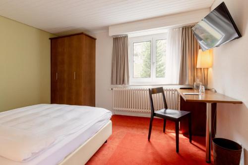 a bedroom with a bed and a desk and a television at Pension Arosa - Self Check-In in Arosa