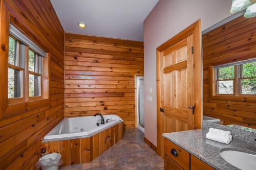 uma casa de banho com uma banheira, 2 lavatórios e uma parede de madeira em Cozy Bear Chalet em McHenry
