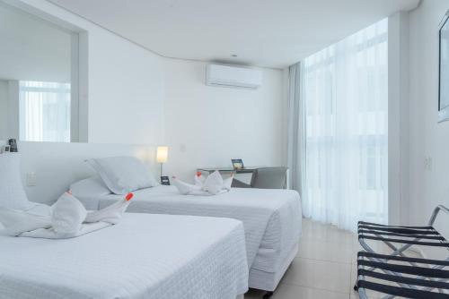 two beds in a white room with two chairs at Hotel Brisa Praia Pajuçara in Maceió