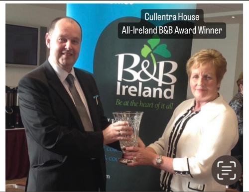 a man and woman holding a glass in front of a sign at Cullentra House in Cushendall
