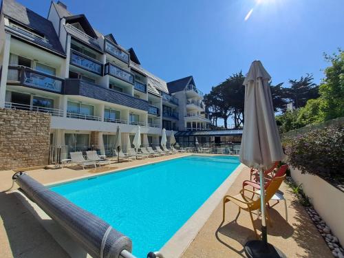 een zwembad met een parasol en stoelen naast een gebouw bij Le Churchill Hôtel & Spa in Carnac