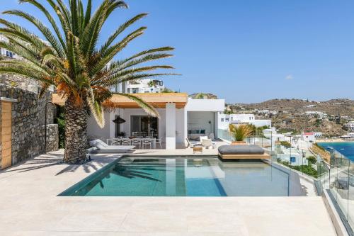 a villa with a swimming pool and a palm tree at Villa Lilium II - Sanctuary overlooking Psarou Bay in Psarou