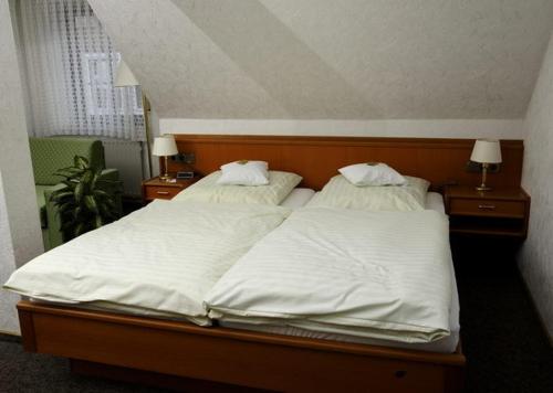 a bedroom with two beds with white sheets and two lamps at Hotel Restaurant Pempel in Großalmerode