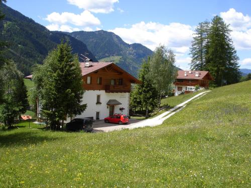 Una casa con un coche rojo aparcado junto a una colina cubierta de hierba. en Cësa Gravina Suaut, en Ortisei