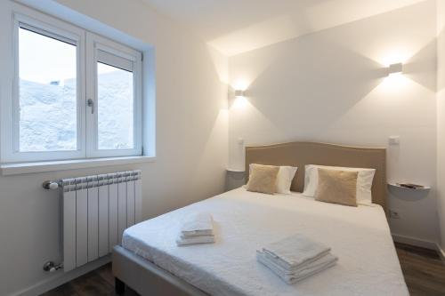 a bedroom with a bed with white sheets and a window at Dona Emília Studio Apartments in Viana do Castelo