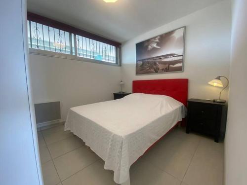 une chambre avec un lit blanc et une tête de lit rouge dans l'établissement Appart 408, Héliopolis K au village naturiste, au Cap d'Agde