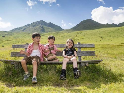 three children sitting on a bench in a field at Bio Aparthotel Blaslahof in Valle Di Casies