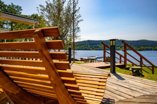 a wooden bench sitting on top of a boardwalk next to a lake at Amenity Hotel & Resort Lipno in Lipno nad Vltavou