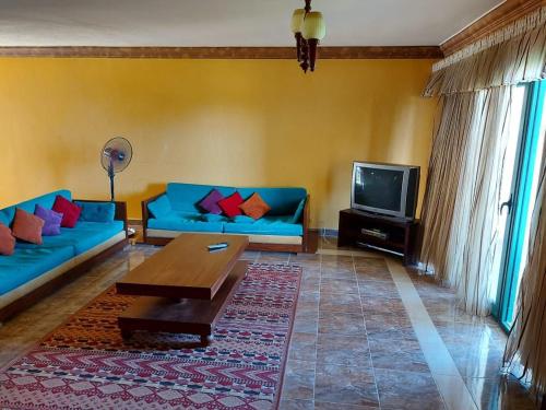 sala de estar con sofás azules y TV en Chalet in Mena 4-North Coast, en Dawwār ‘Abd al ‘Aţī Abū ‘Ajūz
