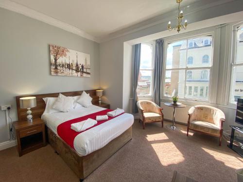 a bedroom with a bed and two chairs and windows at The Broadway Hotel in Llandudno