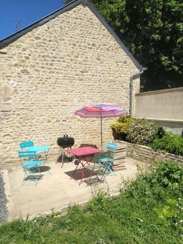 un patio avec une table, des chaises et un parasol dans l'établissement Jolie maison en pierres au calme dans un charmant village aux portes de Bayeux, à Carcagny