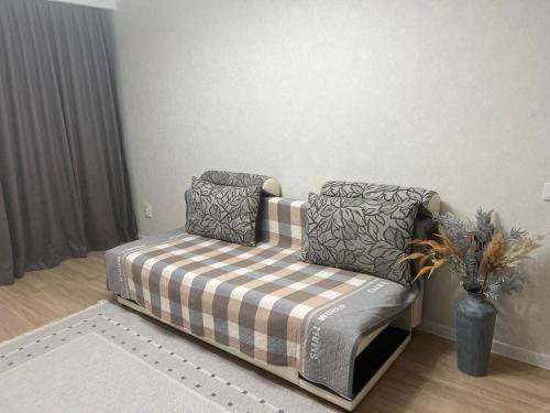 a couch with a plaid blanket and pillows in a room at Квартира в микрорайоне Коктем 3 in Almaty