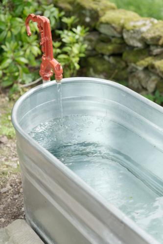 a faucet pouring water into a bucket of water at Eastside - Architect designed retreat with wood-fired sauna in Penicuik