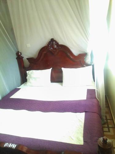 een slaapkamer met een houten bed met witte lakens bij City Max hotel Kabaale in Kabale