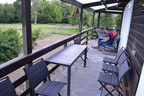 twee personen zitten op een veranda met een tafel en stoelen bij Le Chalet du Gégé in Bouillon
