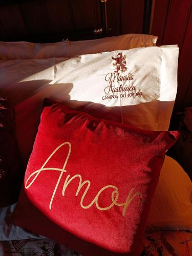 a red pillow sitting on a bed with a bag at Mansão Austríaca Guesthouse in Campos do Jordão