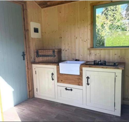 a kitchen with white cabinets and a sink and a window at Cosycoopmiskineggs in Llantrisant