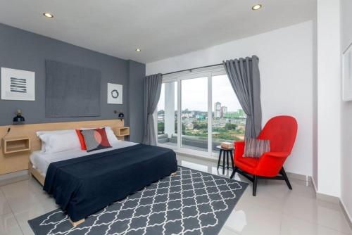 a bedroom with a bed and a red chair and a window at Gallery suites and Apartments in Accra