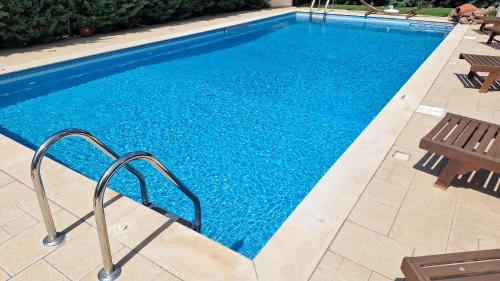 a swimming pool with blue water and two benches at Kantza Private Pool Project, near metro, A 60sm lux pool for your use only in Leondárion
