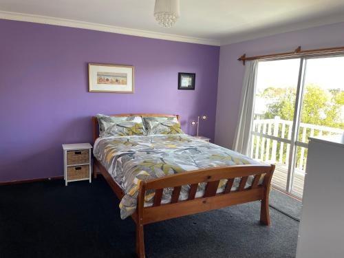 a bedroom with a bed with purple walls and a window at Live Large in the Village in Havelock North