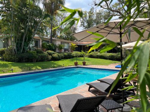 a swimming pool with two chairs and an umbrella at Casa Gabriela para gozar con los tuyos-piscina con calefacción in Cuernavaca