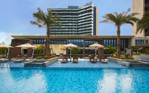 a swimming pool with chairs and umbrellas and a building at Renaissance Haikou Hotel in Haikou
