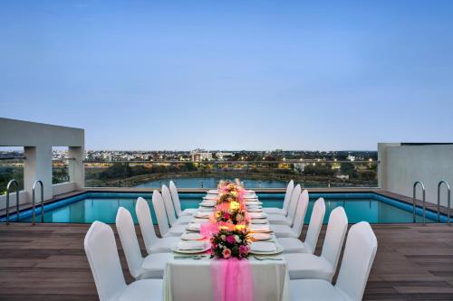 uma mesa longa com cadeiras brancas e uma piscina em Ramada Encore by Wyndham Indore Nipania em Indore