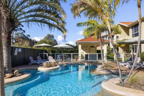 a pool with palm trees and chairs in a yard at Martys Little Beach NO. 4 Ground Floor Apartment with Heated Pool access in Nelson Bay