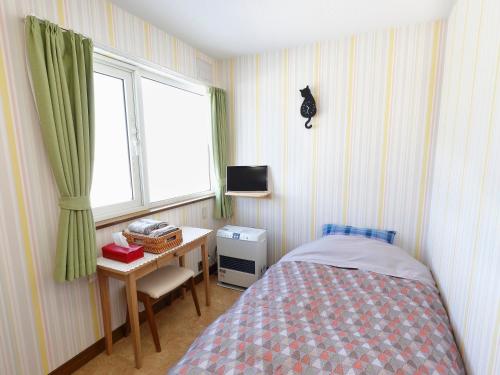 a bedroom with a bed and a desk and a window at Pension Ken&Mary in Biei