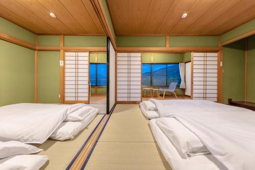 two beds in a room with windows at 天然温泉&絶景露天風呂付き貸切宿のんびり一非日常空間を愉しむ一10人でも広々 in Izu