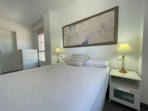 a white bedroom with a large white bed and two lamps at Seaside Apartment Retreat in Benicàssim