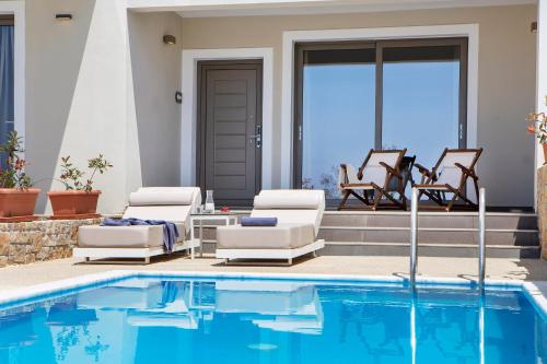 a swimming pool with two lounge chairs next to a house at Ajul Luxury Hotel & Spa Resort, a Registry Collection Hotel in Agia Paraskevi