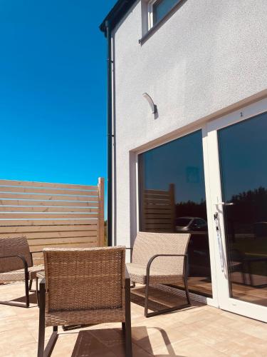 a patio with three chairs and a table and glass doors at BALTICO Domki Letniskowe in Sarbinowo