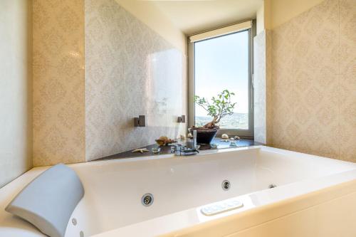 La salle de bains est pourvue d'une grande baignoire blanche et d'une fenêtre. dans l'établissement Deluxe Maisonette With Shared Pool 2#, à Anavyssos
