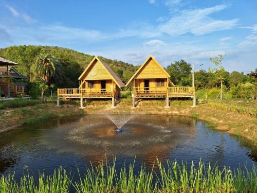 a small pond with two cottages in the background at คูณ-เนื่อง ฟาร์ม สเตย์ หัวหิน Koon & Nueang Farm Stay Hua Hin in Ban Bo Fai