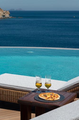two glasses of wine and a pizza on a table next to a pool at Etesians Suites & Villas in Super Paradise Beach