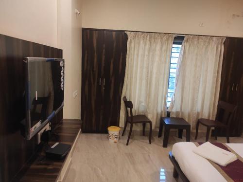 a hotel room with a tv and a bed and chairs at Hotel Deepak Executive, Ganpatipule in Ganpatipule