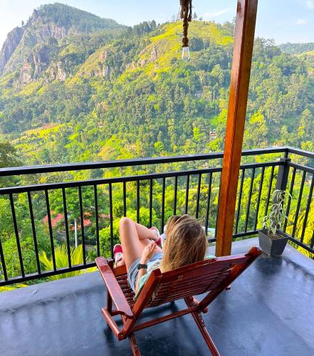 Eine Frau sitzt auf einem Stuhl auf einem Balkon und blickt auf einen Berg. in der Unterkunft The Peak Ella in Ella