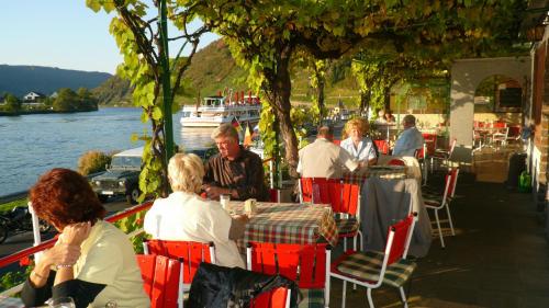 a group of people sitting at tables at a restaurant by the water at Hotel Haus Burg Metternich in Beilstein