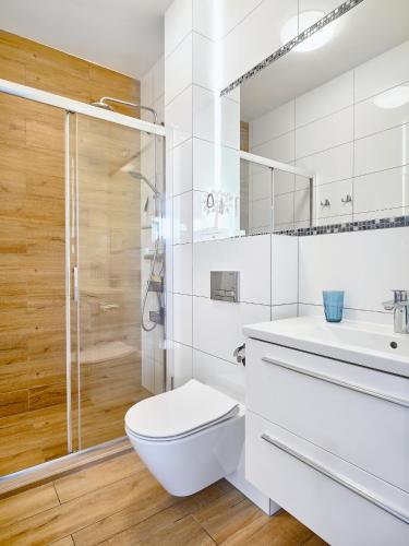 a white bathroom with a toilet and a shower at Villa Łeba Pokoje & Apartamenty in Łeba