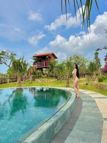 a woman standing next to a swimming pool at a resort at BlackPink Homestay Hồ Tràm in Xóm Trương Quít