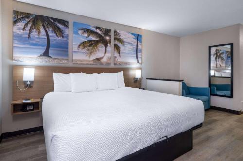 a large white bed in a hotel room with palm trees at Days Inn & Suites by Wyndham Commerce in Commerce