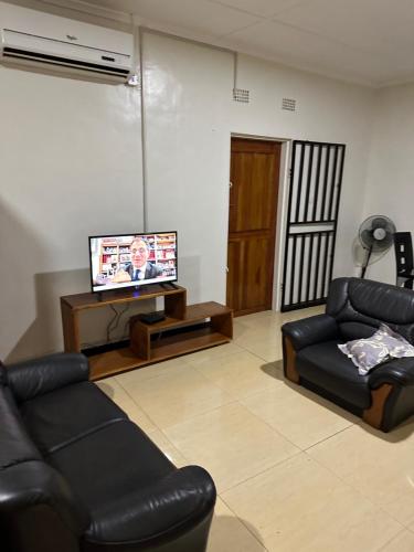 uma sala de estar com duas cadeiras de couro e uma televisão em Axe Apartments em Solwezi