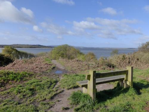 a wooden bench sitting on top of a hill next to a river at Rockley Park Private Holiday Homes in Poole