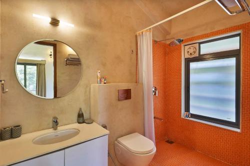 a bathroom with a toilet and a sink and a mirror at StayVista's Amoda Villa - Near Venna Lake, Amidst Farmland with Jacuzzi and Indoor Activities in Mahabaleshwar